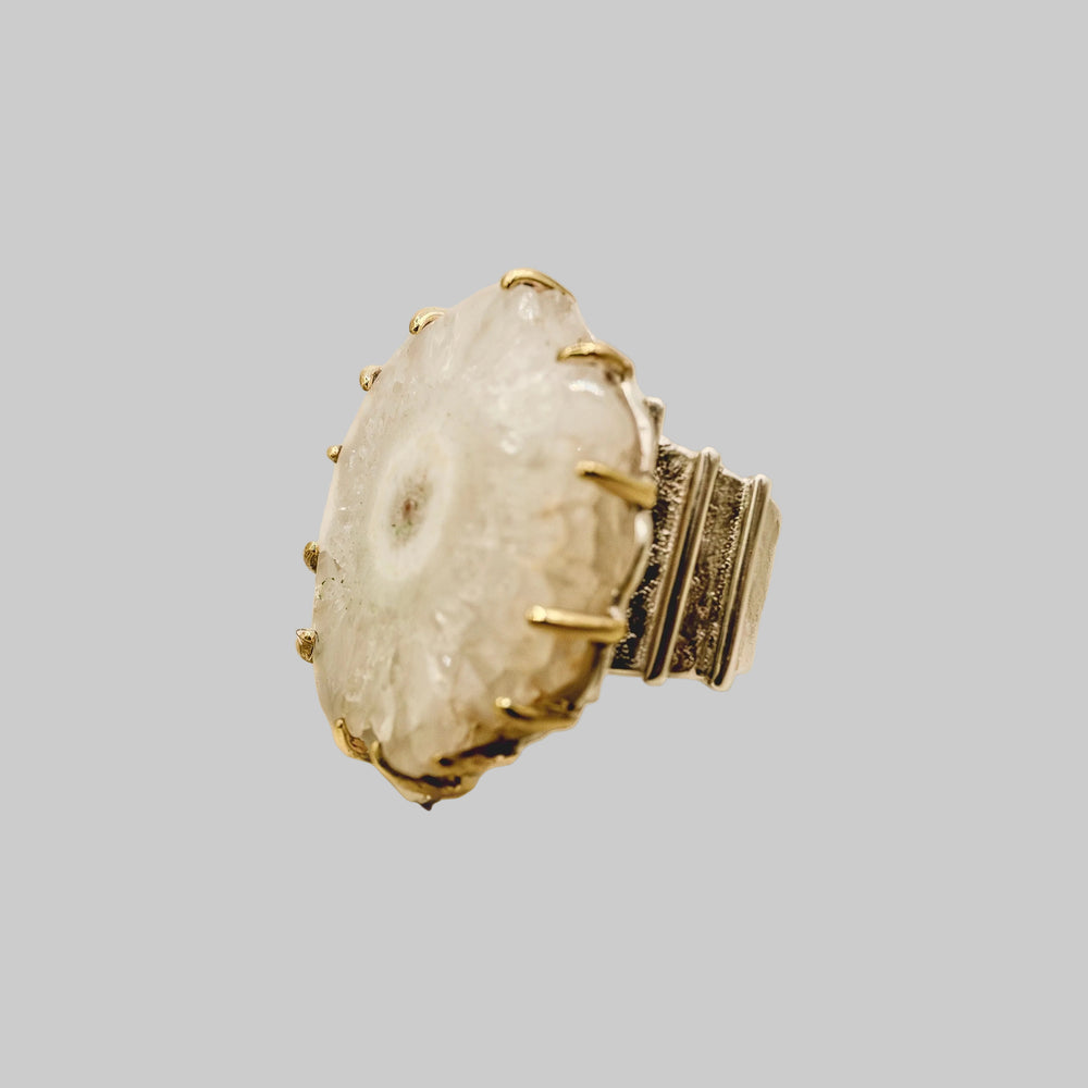 Ring with a textured stone and gold accents on a beige background