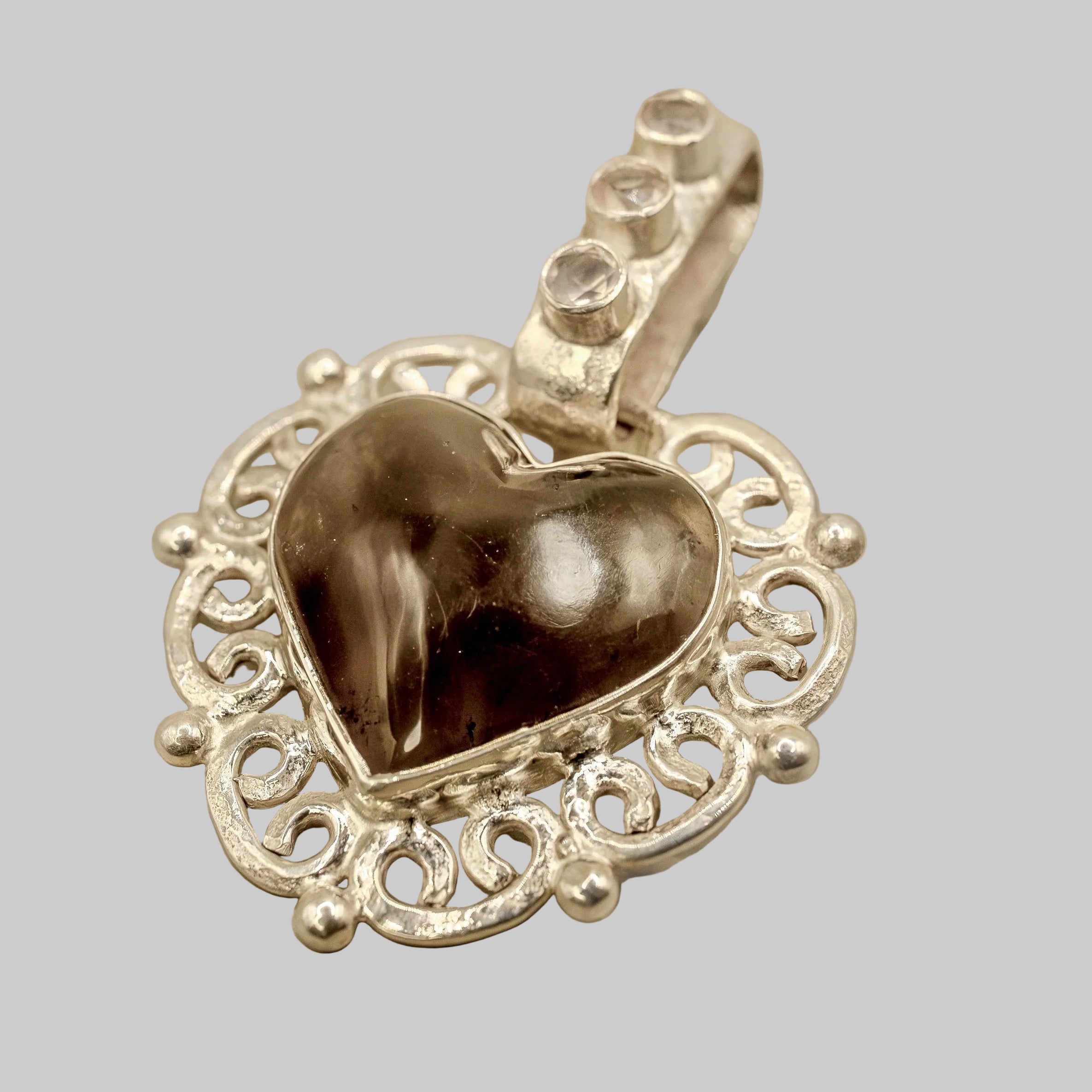 Heart-shaped pendant with intricate silver design on a beige background