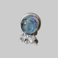 Silver ring with a blue gemstone and dangling crystals on a light gray background