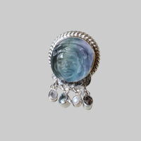 Silver ring with a blue gemstone and dangling crystals on a light gray background