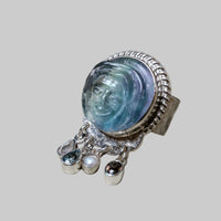 Silver ring with face design and dangling elements on a light gray background