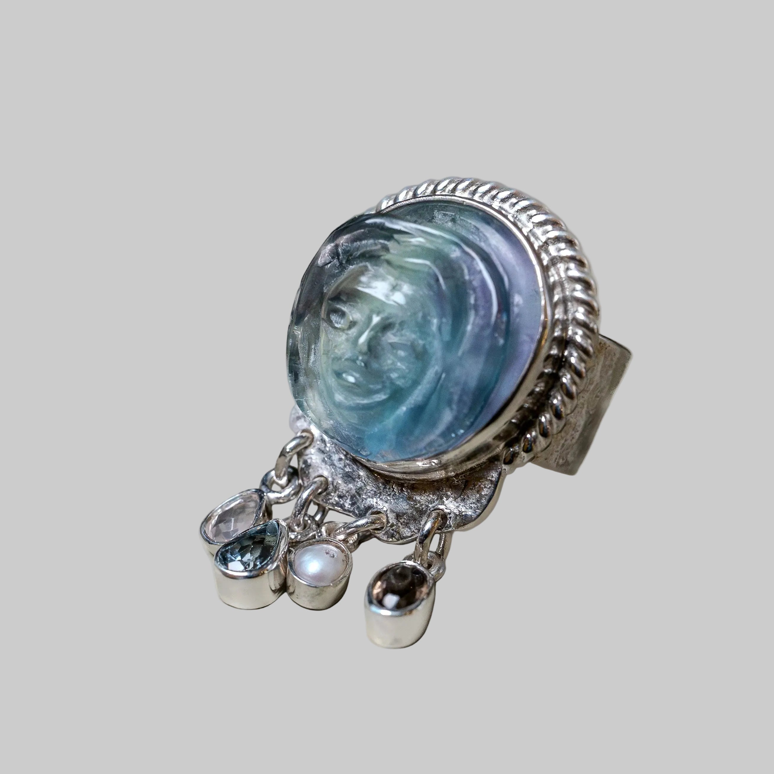 Silver ring with face design and dangling elements on a light gray background