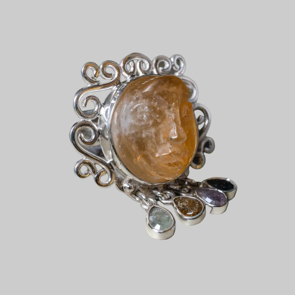 Silver ring with a large amber stone and smaller gemstones on a beige background