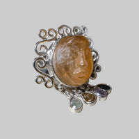 Silver ring with a large amber stone and smaller gemstones on a beige background