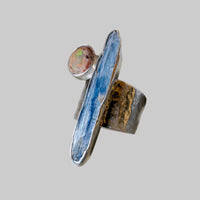 Silver ring with a large blue stone and smaller round stone on a light gray background