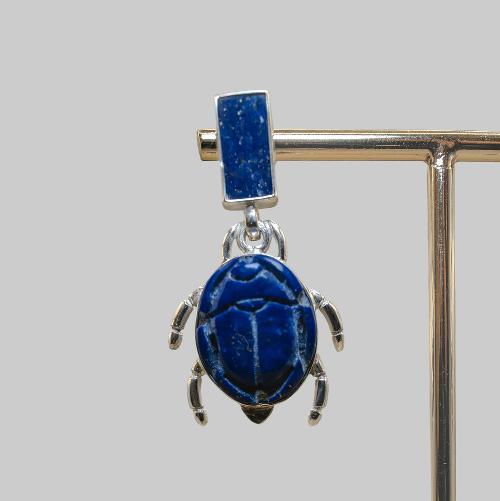 Blue stone pendant on a stand against a beige background