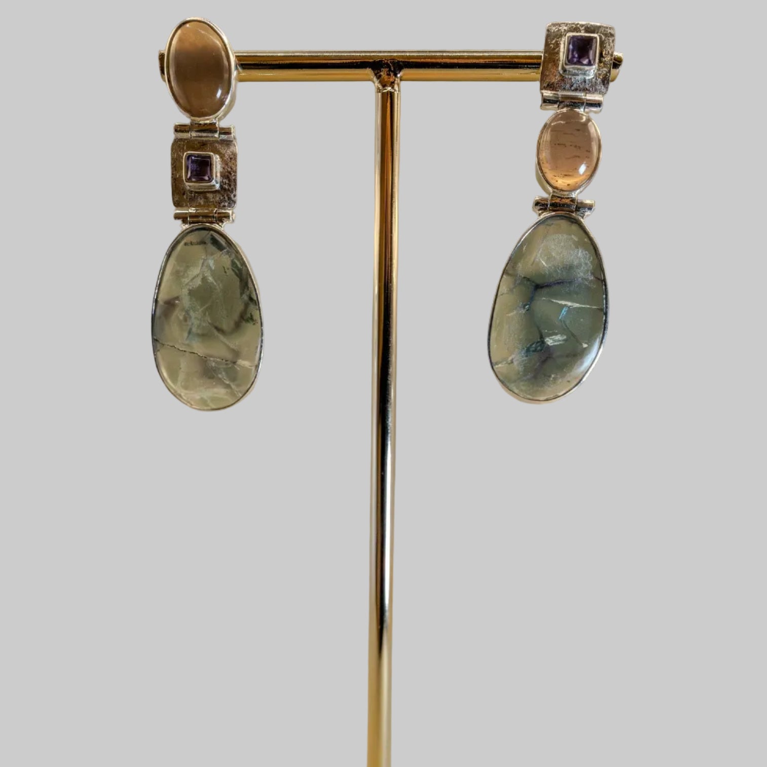 Pair of earrings on a gold stand with a wooden base against a beige background