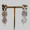 Pair of ornate earrings with gemstones on a stand against a neutral background