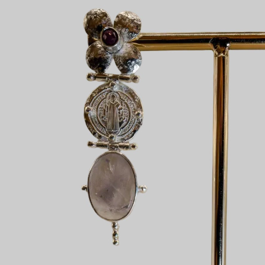 Pair of earrings on a wooden stand against a beige background