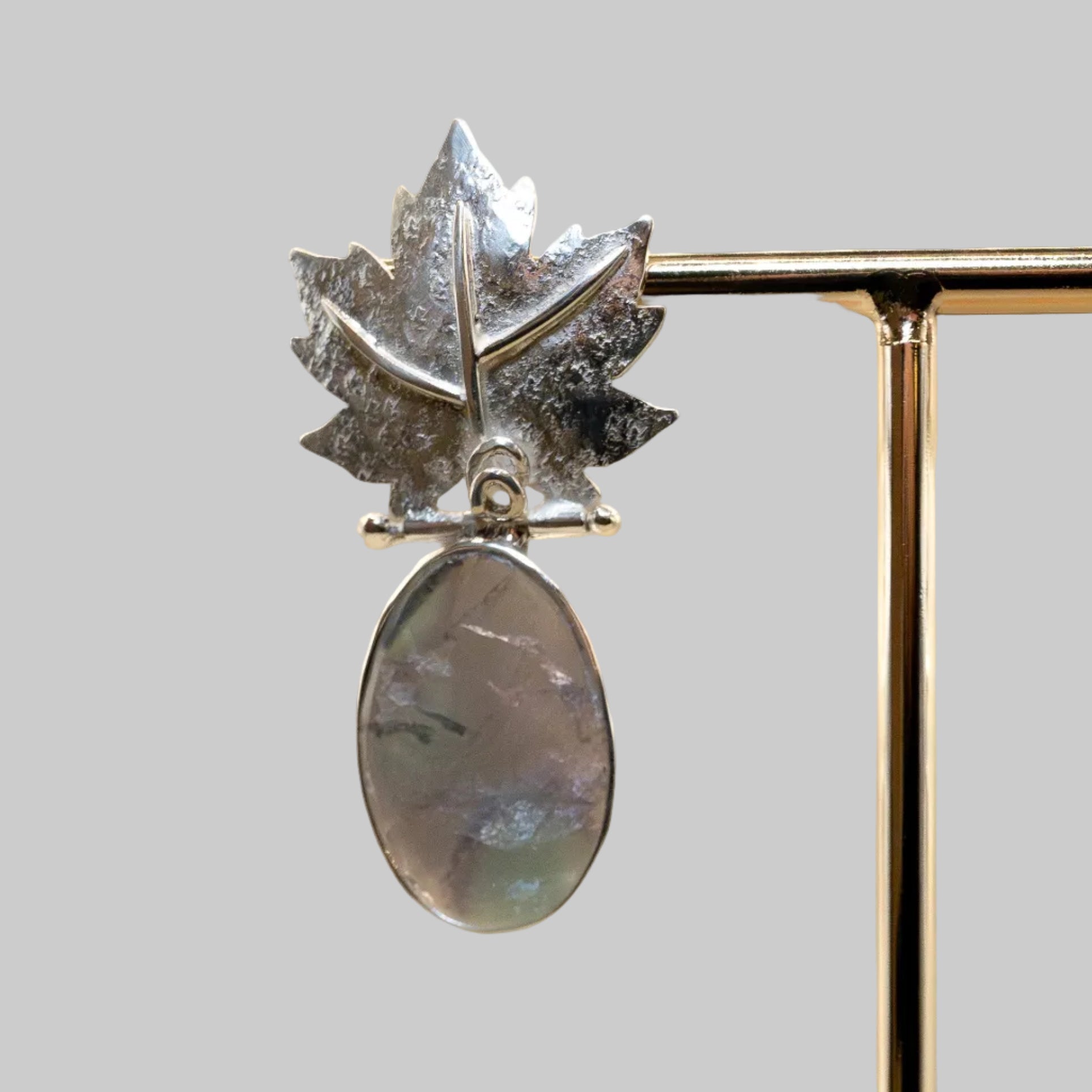 Silver leaf-shaped earring with a rainbow moonstone on a beige background