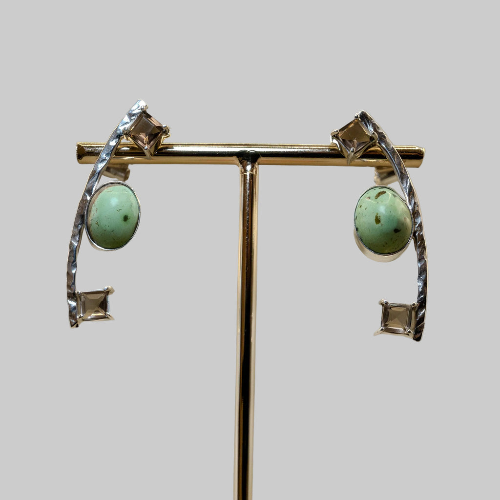 Pair of earrings with turquoise stones and silver accents on a stand against a beige background