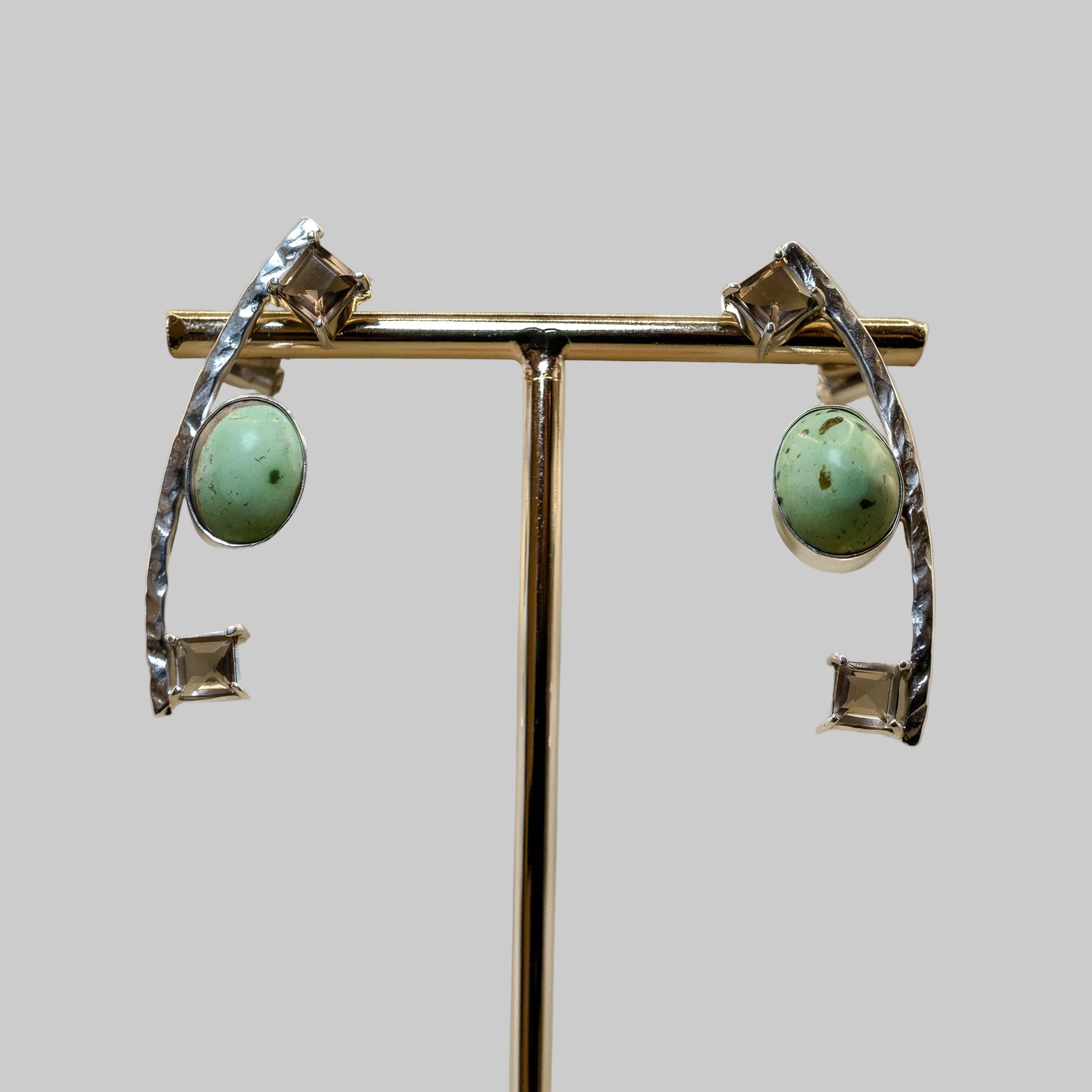 Pair of earrings with turquoise stones and silver accents on a stand against a beige background