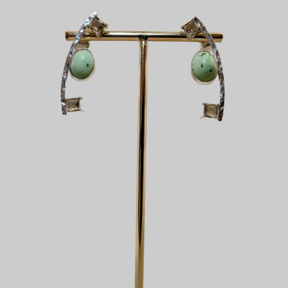 Pair of earrings on a gold stand with a wooden base against a beige background