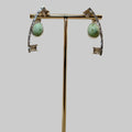 Pair of earrings on a gold stand with a wooden base against a beige background