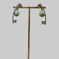 Pair of earrings on a gold stand with a wooden base against a beige background