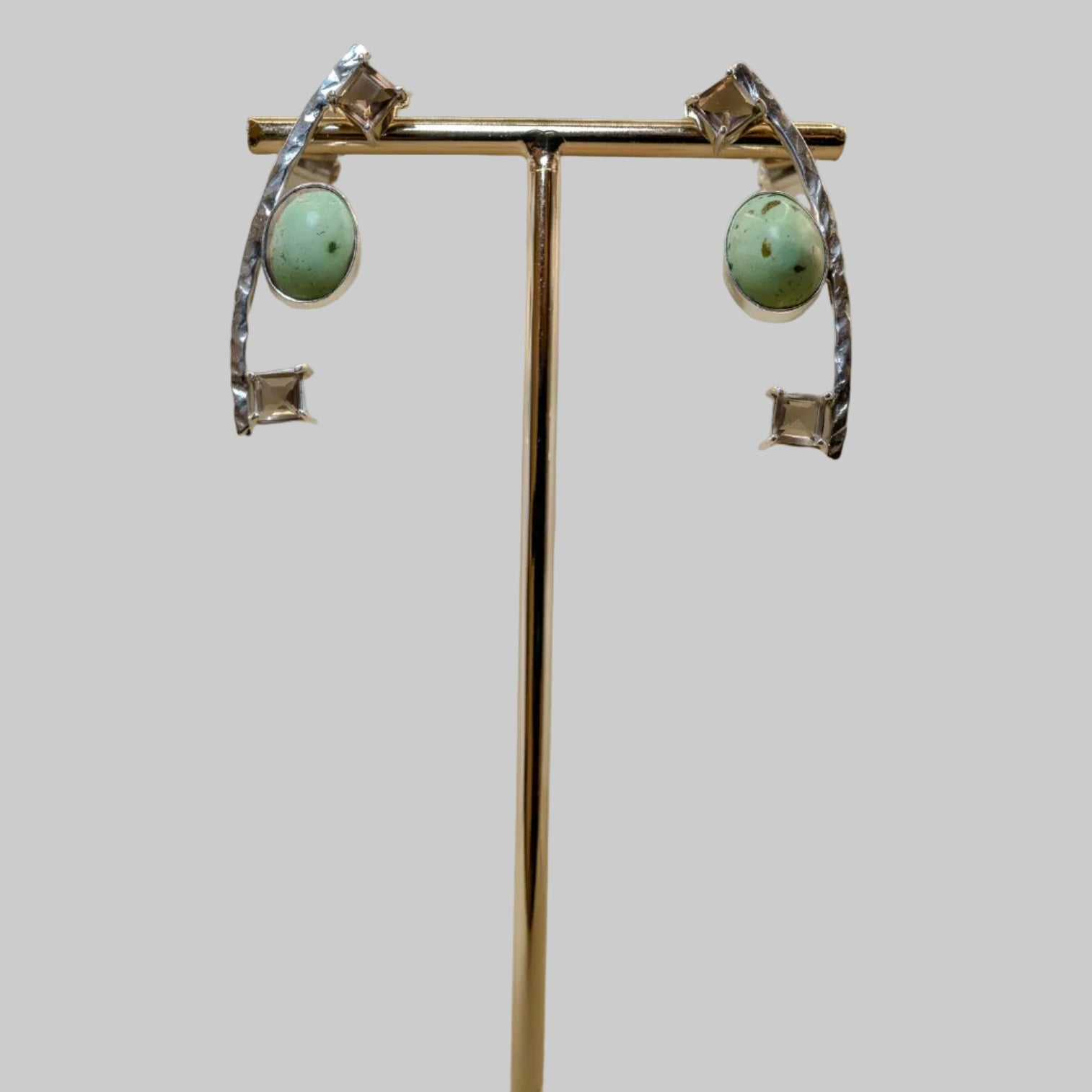 Pair of earrings on a gold stand with a wooden base against a beige background