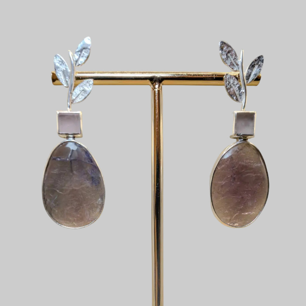 Pair of earrings on a gold stand against a beige background
