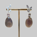 Pair of earrings on a gold stand against a beige background