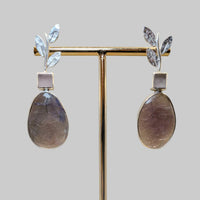 Pair of earrings on a gold stand against a beige background