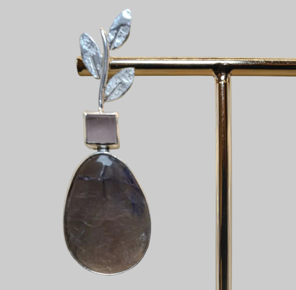 Pair of earrings with teardrop-shaped stones on a stand against a neutral background