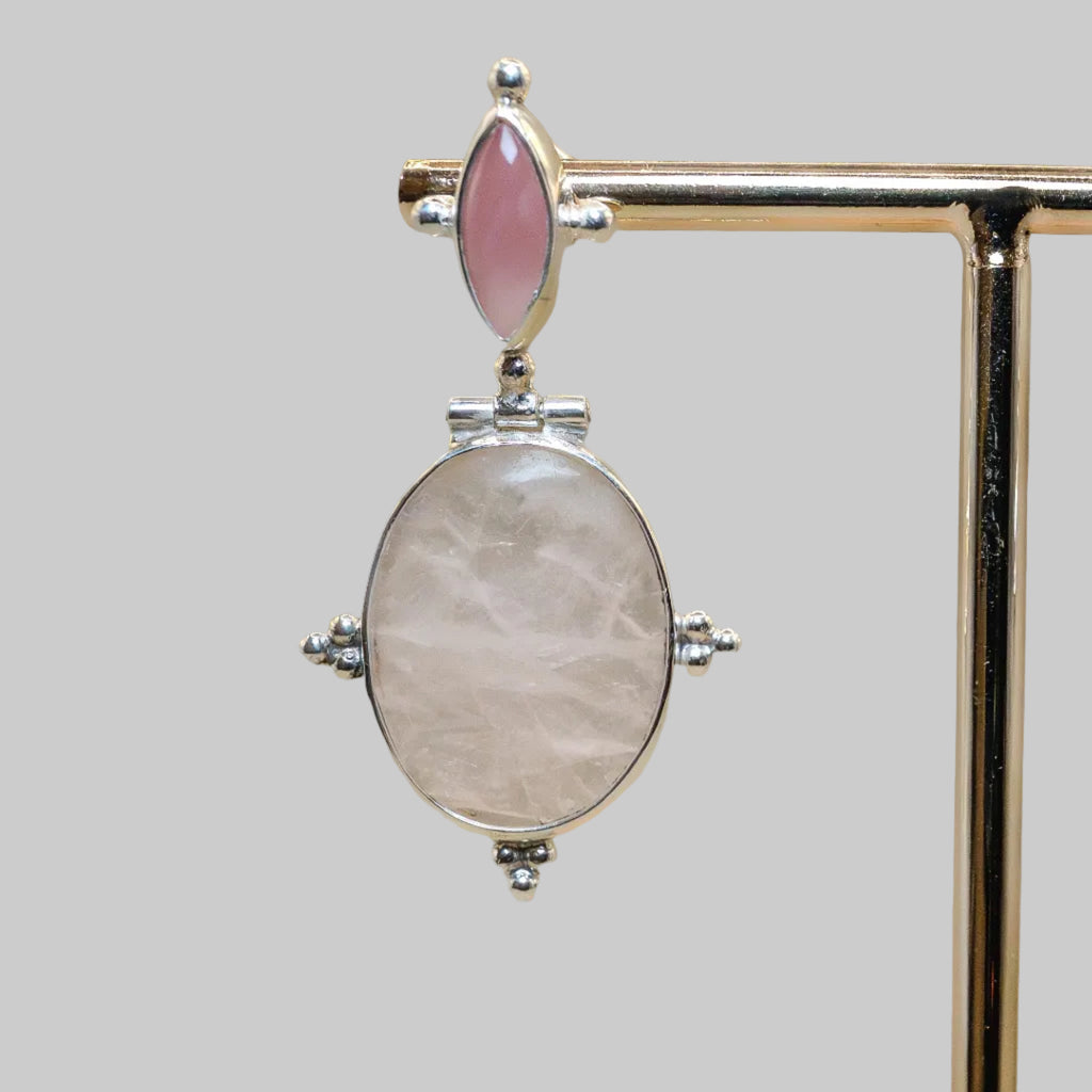 Jewelry pendant with pink gemstone and silver accents on a stand.