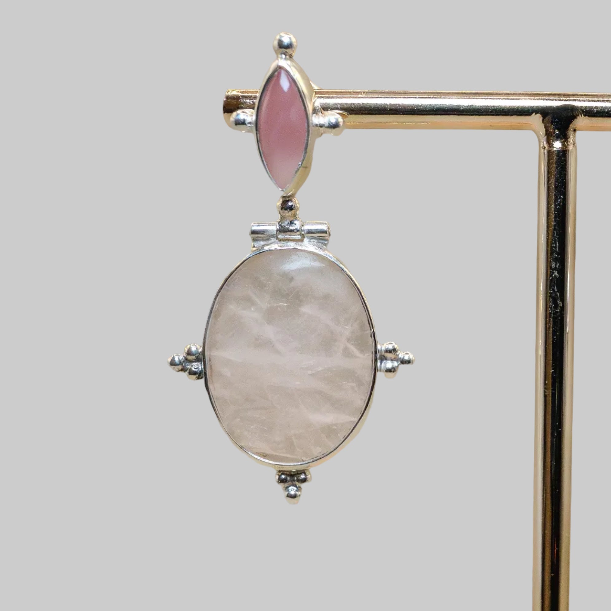 Jewelry pendant with pink gemstone and silver accents on a stand.