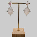 Pair of earrings on a gold stand with a wooden base against a beige background