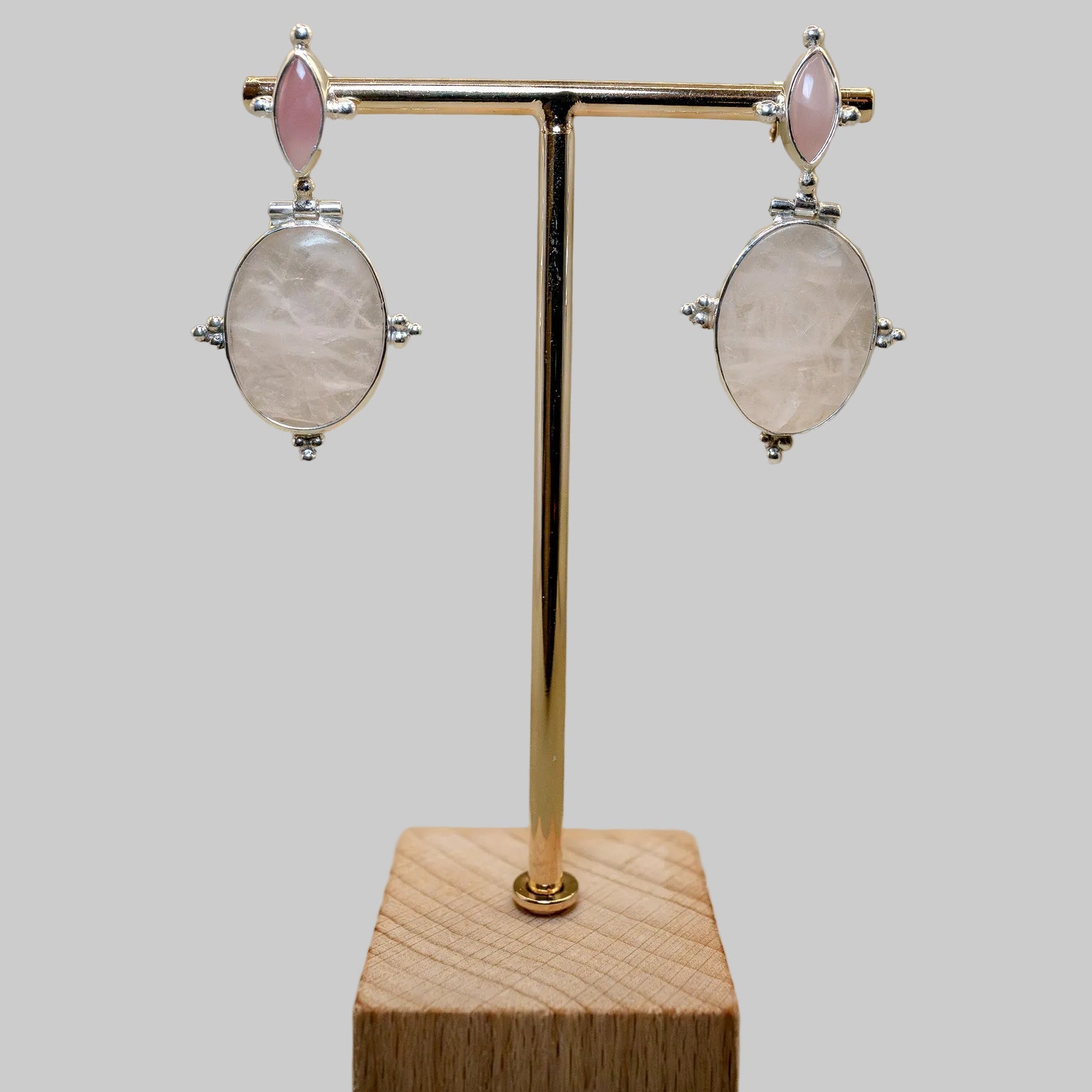Pair of earrings on a gold stand with a wooden base against a beige background