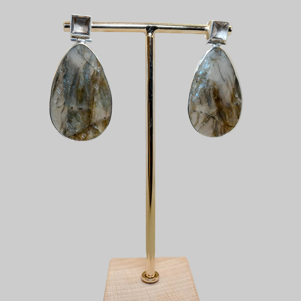 Teardrop-shaped earrings on a gold stand with a wooden base against a beige background