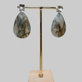 Teardrop-shaped earrings on a gold stand with a wooden base against a beige background