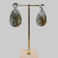 Teardrop-shaped earrings on a gold stand with a wooden base against a beige background