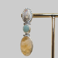 Silver earrings with stone accents on a stand against a beige background