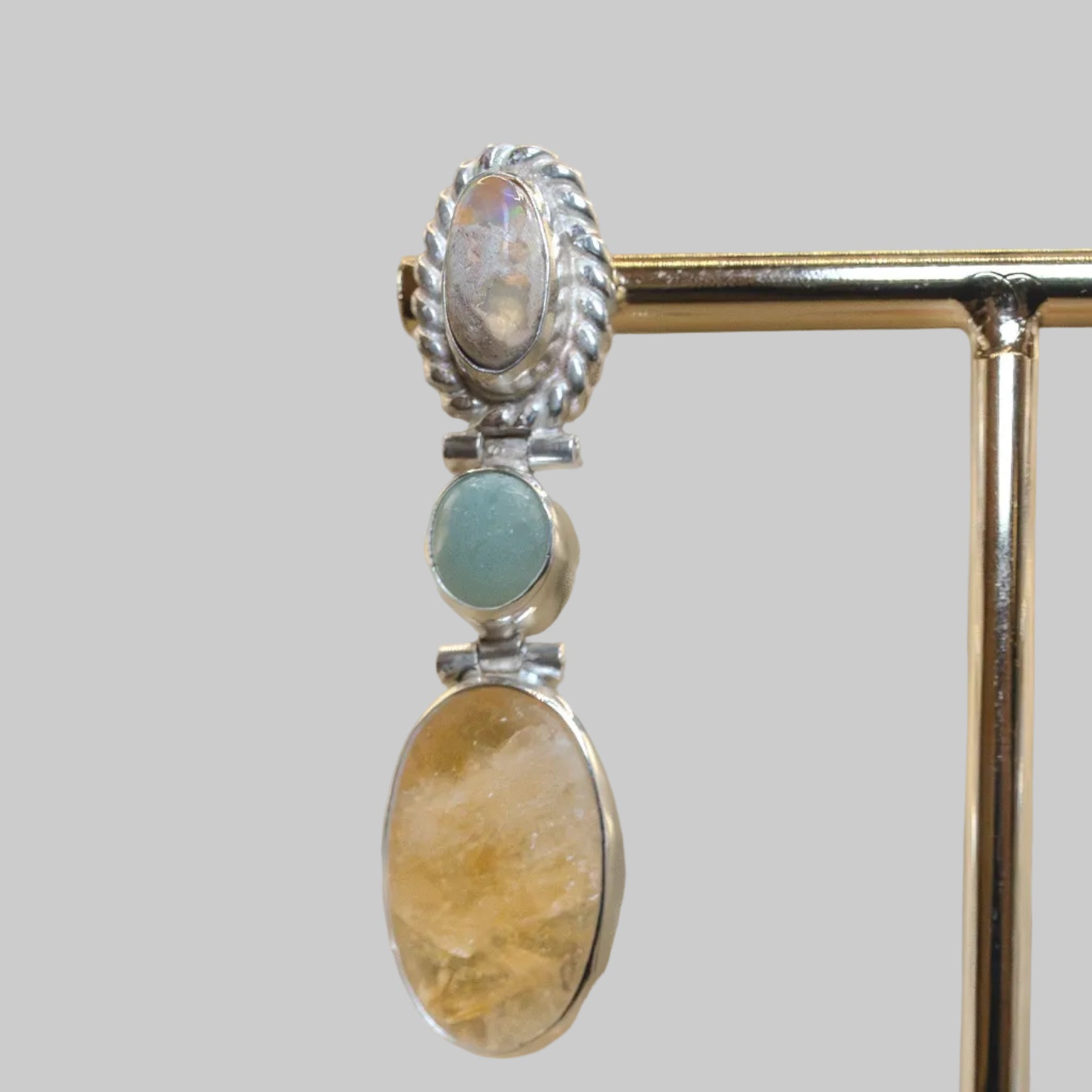 Silver earrings with stone accents on a stand against a beige background