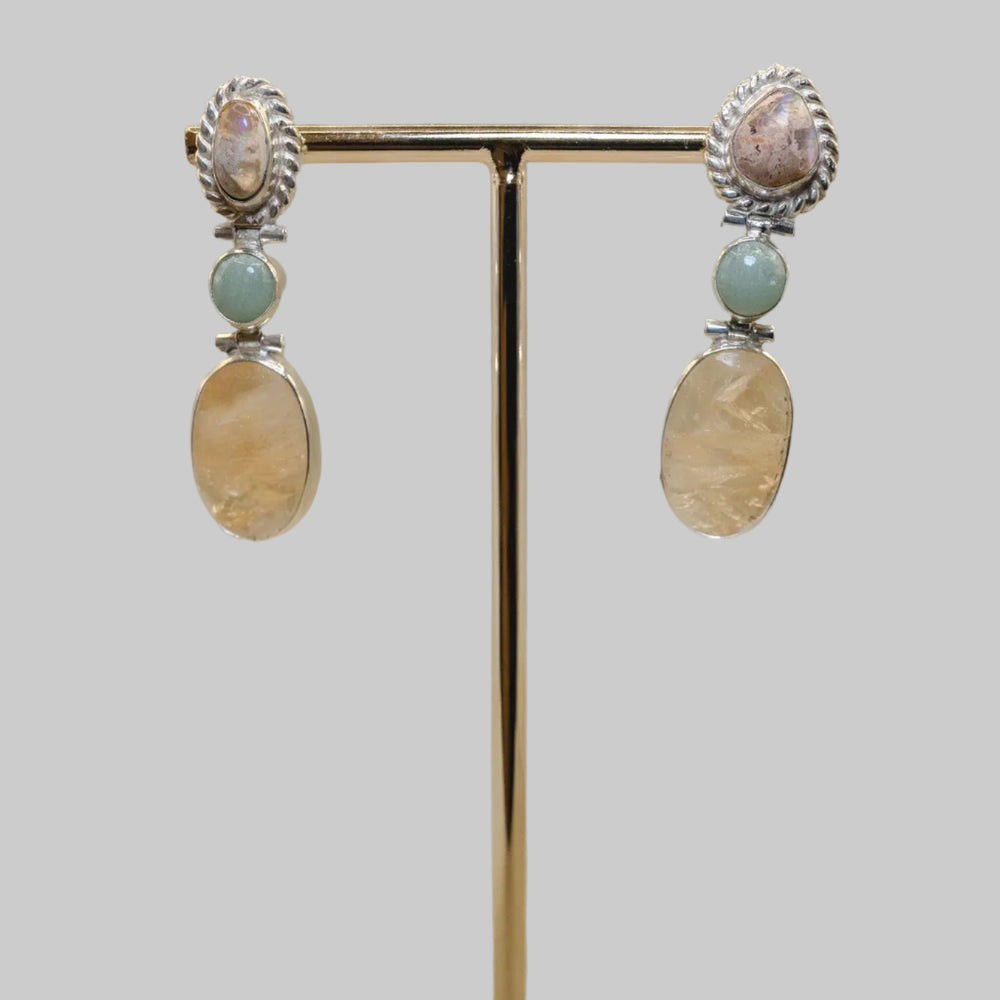 Pair of earrings on a gold stand with a wooden base against a beige background