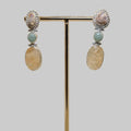 Pair of earrings on a gold stand with a wooden base against a beige background