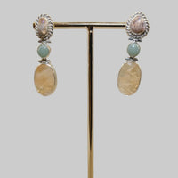 Pair of earrings on a gold stand with a wooden base against a beige background