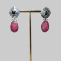 Pair of earrings with pink stones on a gold stand against a beige background