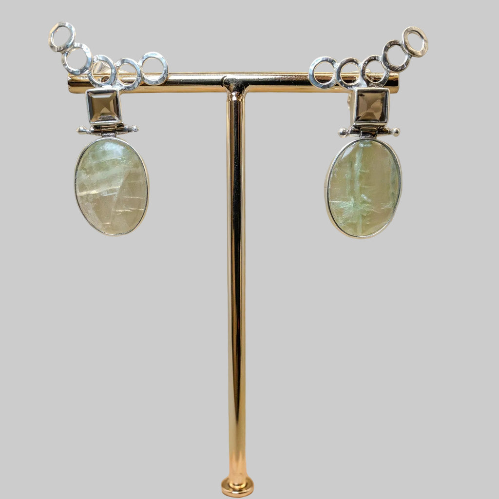 Pair of earrings on a gold stand with a wooden base against a beige background