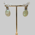 Pair of earrings on a gold stand with a wooden base against a beige background