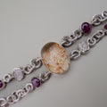 Silver bracelet with a large oval stone and smaller purple stones on a light gray background