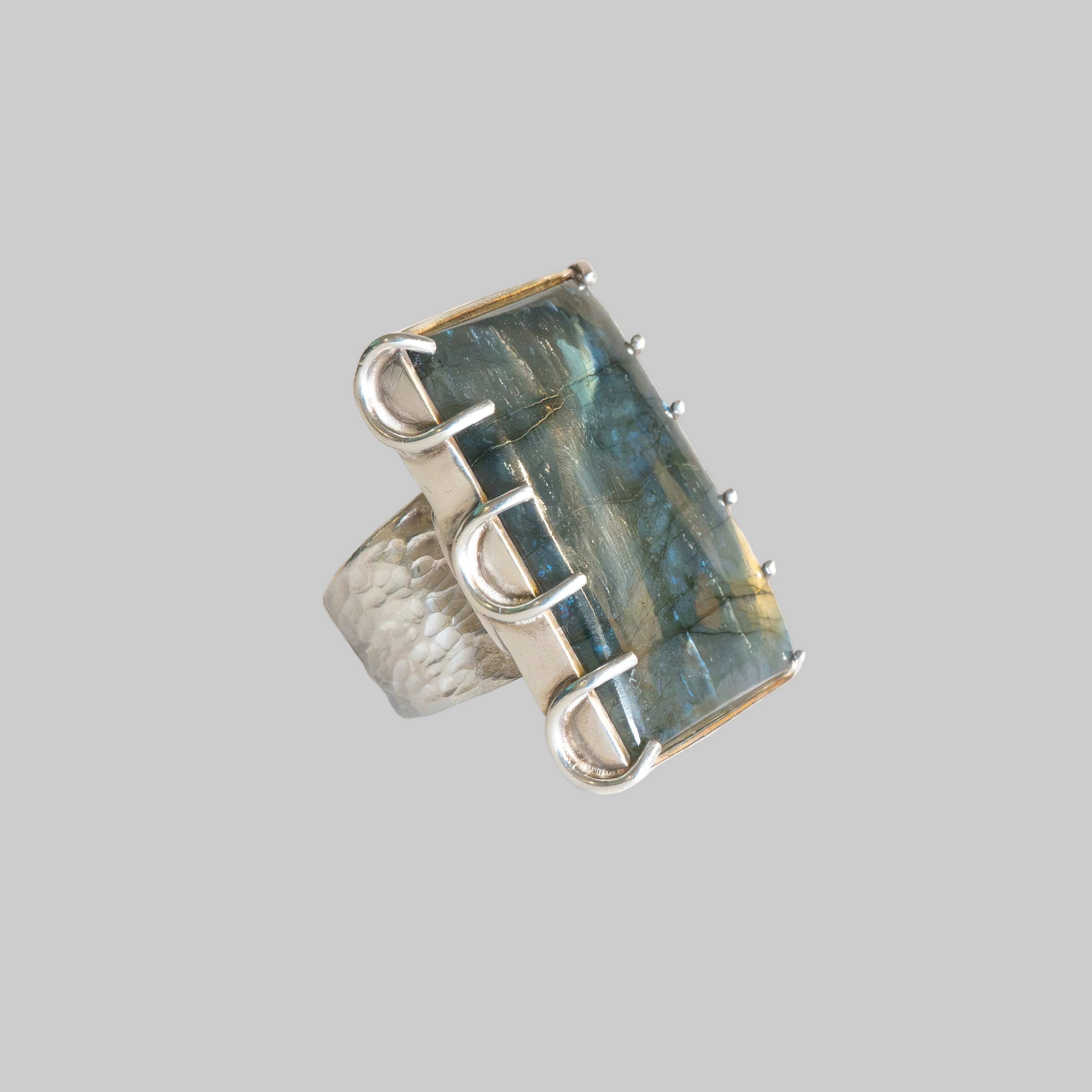 A silver ring featuring a large, rectangular labradorite stone with blue and green flashes, set in a textured sterling silver band.