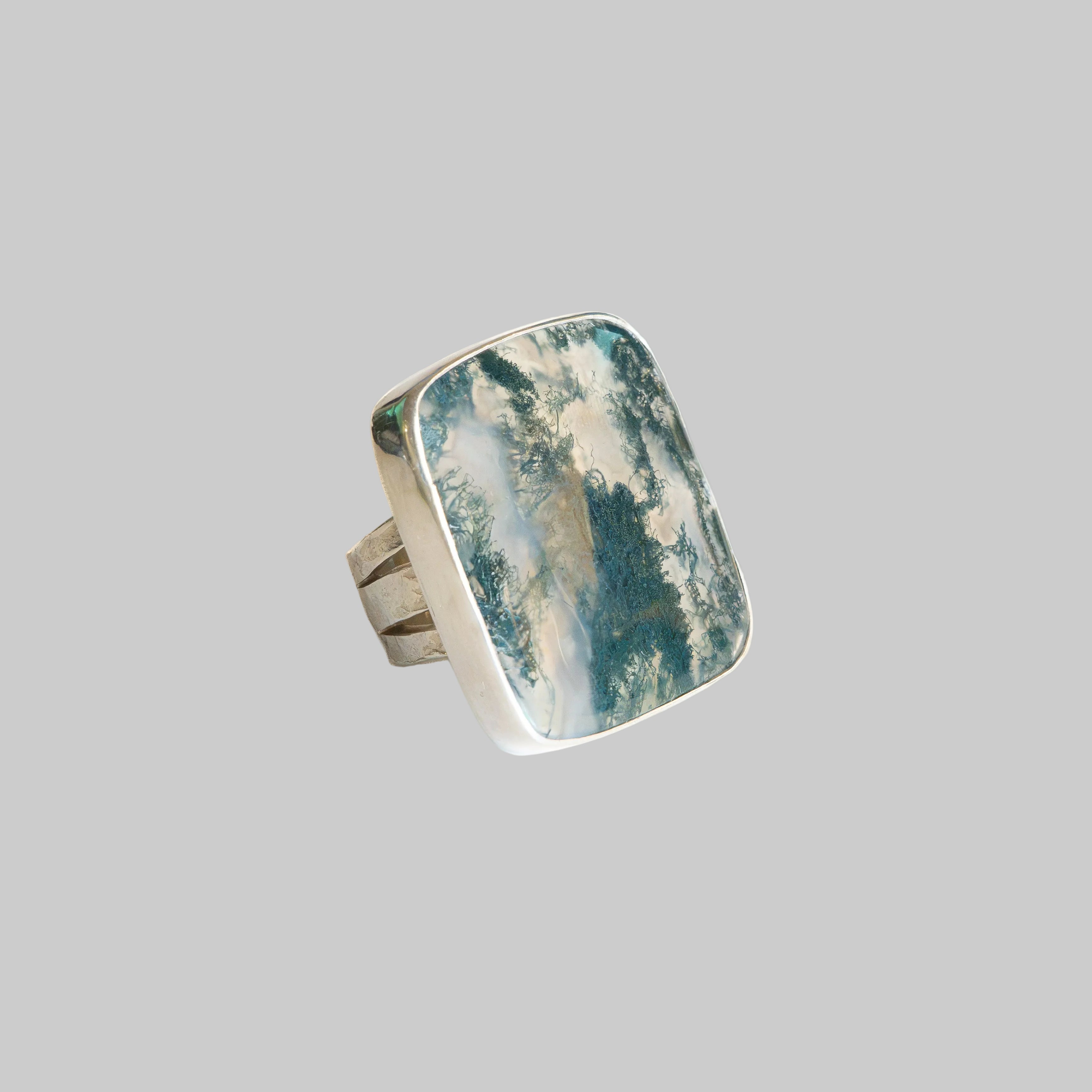 A silver ring featuring a large, rounded rectangular cabochon stone with a marbled pattern of teal, blue, and white.