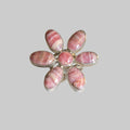 A flower-shaped ring featuring six oval pink and white banded stone petals with a polished silver-tone metal setting, displayed on a light beige background.