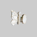 A silver butterfly ring with a white mother-of-pearl oval back and a small round pearl accent, photographed on a neutral cream background.
