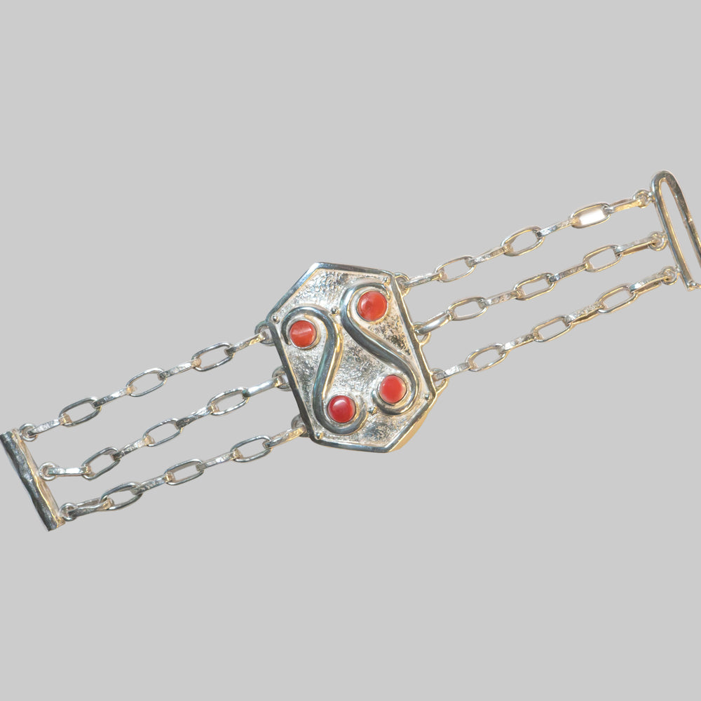A silver-toned multi-strand chain bracelet with a central shield-shaped clasp featuring four red cabochon stones, photographed on a plain white background.