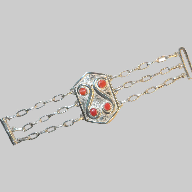 A silver-toned multi-strand chain bracelet with a central shield-shaped clasp featuring four red cabochon stones, photographed on a plain white background.