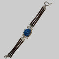 A multi-strand bracelet featuring dark brown leather cords, a central oval blue lapis lazuli stone in a silver-toned bezel, and silver-toned metal connectors and clasp.