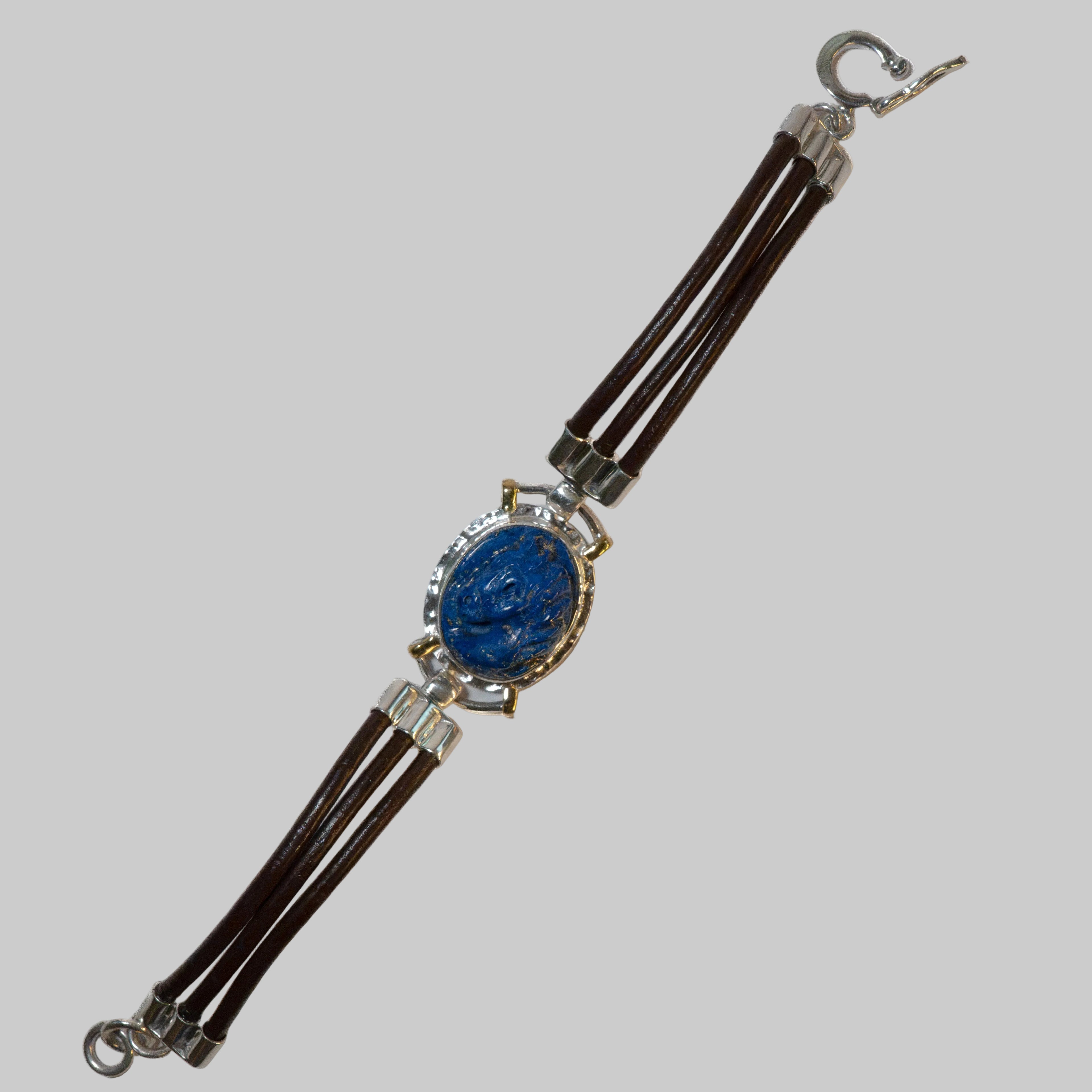 A multi-strand bracelet featuring dark brown leather cords, a central oval blue lapis lazuli stone in a silver-toned bezel, and silver-toned metal connectors and clasp.