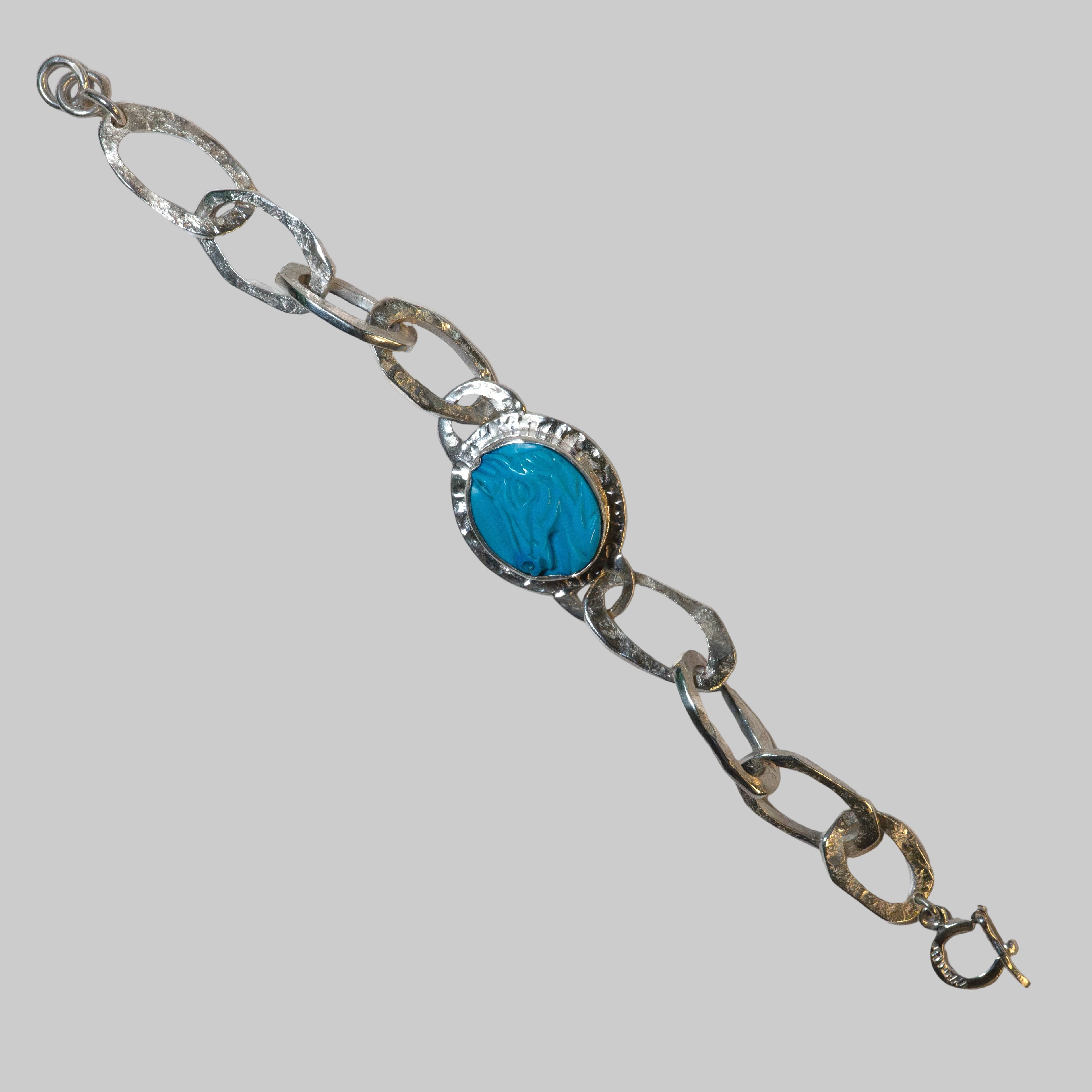 A handmade silver chain bracelet featuring a central oval turquoise cabochon set in a textured silver bezel, displayed diagonally on a plain white background.