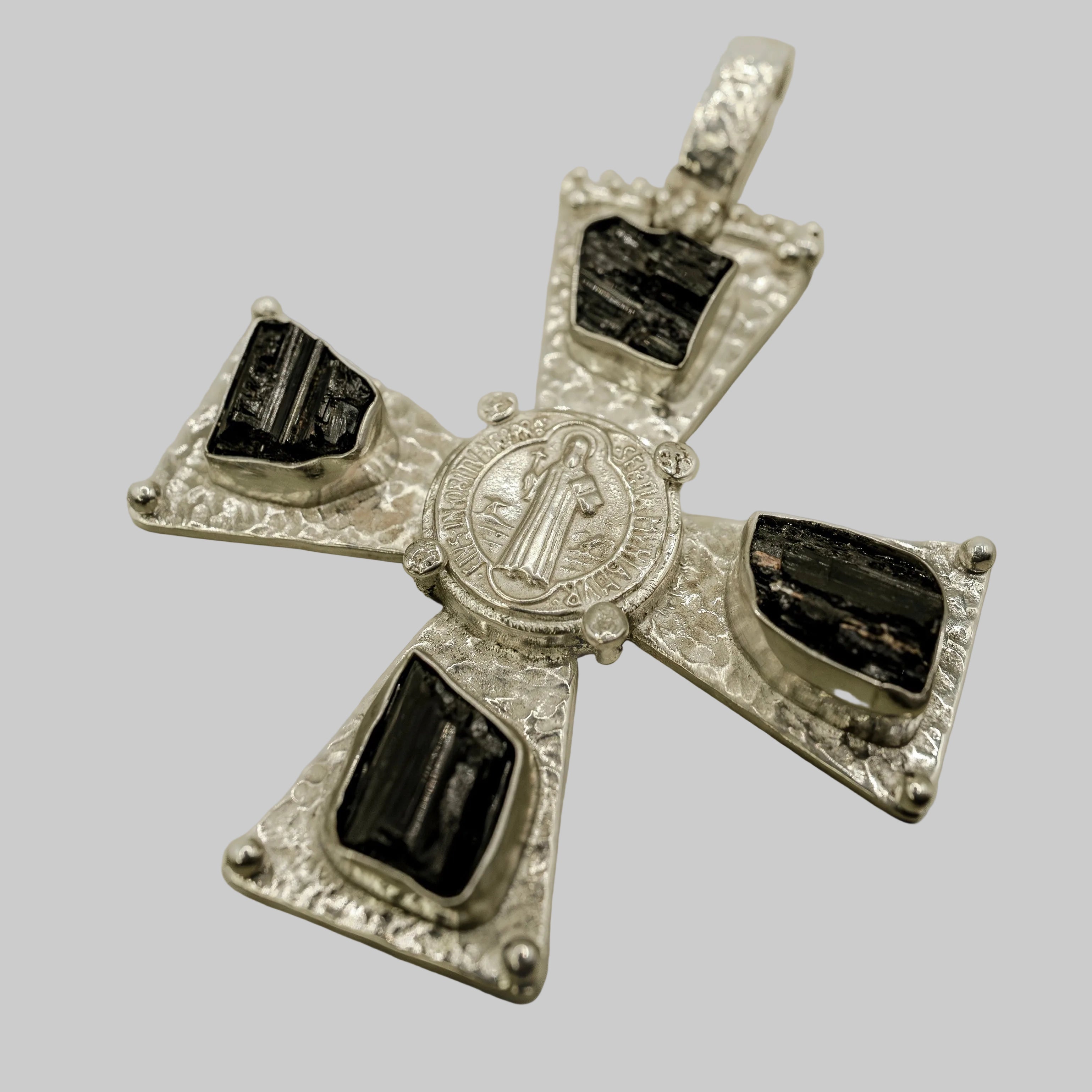 Silver cross pendant with black stones on a beige background